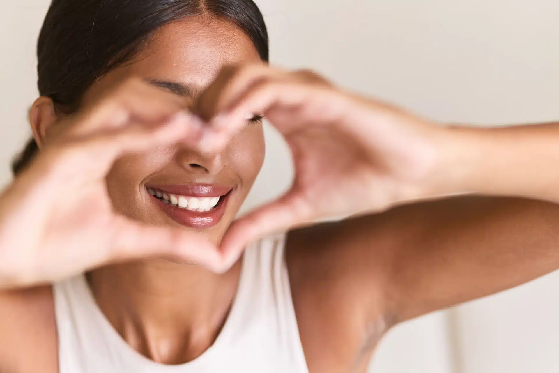 Smilende kvinne som lager et hjerte med hendene sine som rammer inn munnen hennes med hvite tenner etter tannbleking hos tannlege